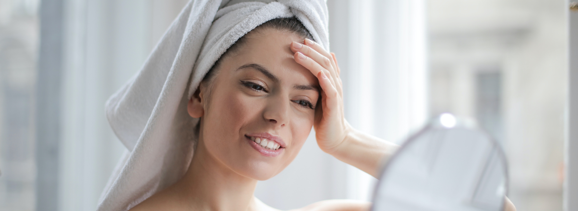 Woman after shower looking at her face in a handheld mirror
