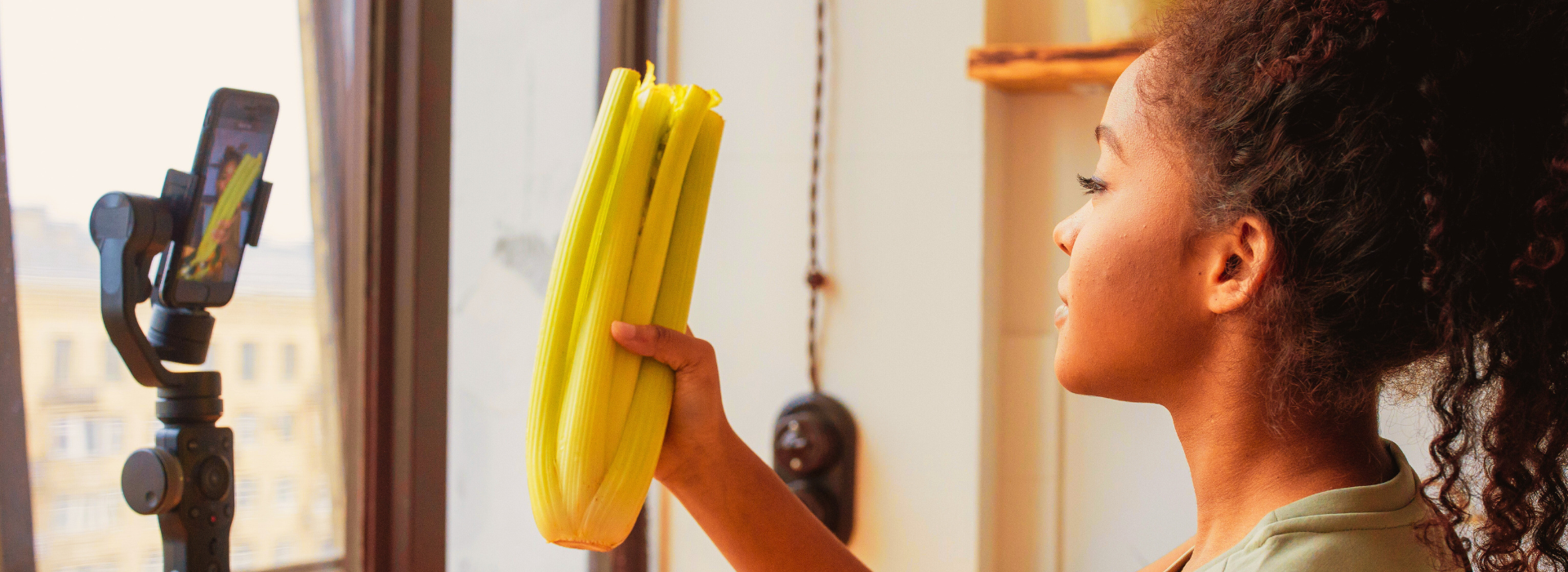 Girl holding a hand of celery while filming herself 