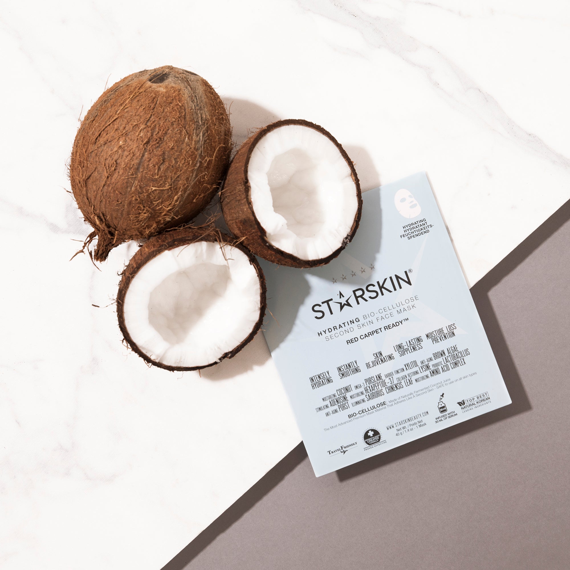 Atmospheric image of the red carpet ready mask. On the left top of the product are some coconuts. The background is part marble and part grey
