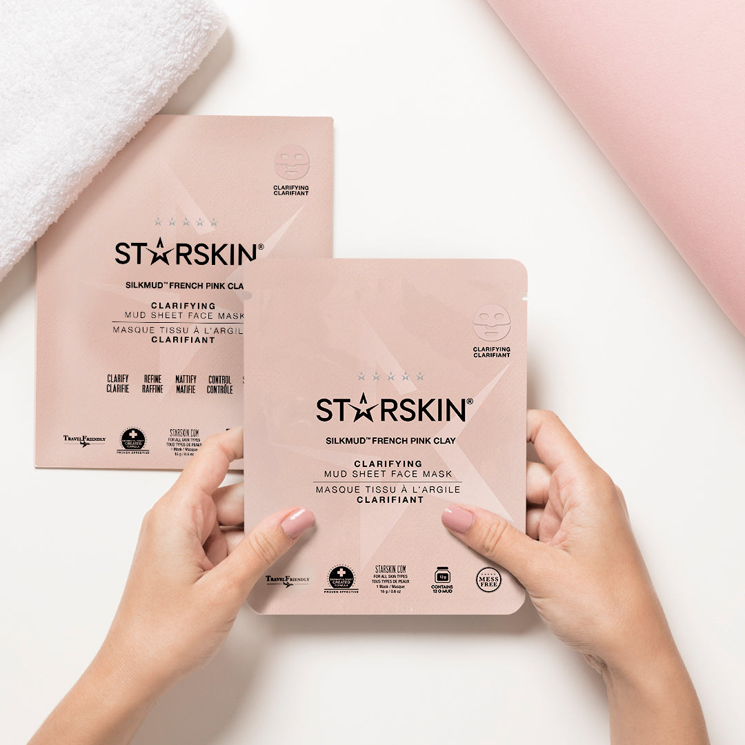 Starskin's French Pink Clay product packaging on the left of the image. In the middle is the product sachet being held in someones hands. In the top left corner there is a towel. The background of the image is part white part pink. 