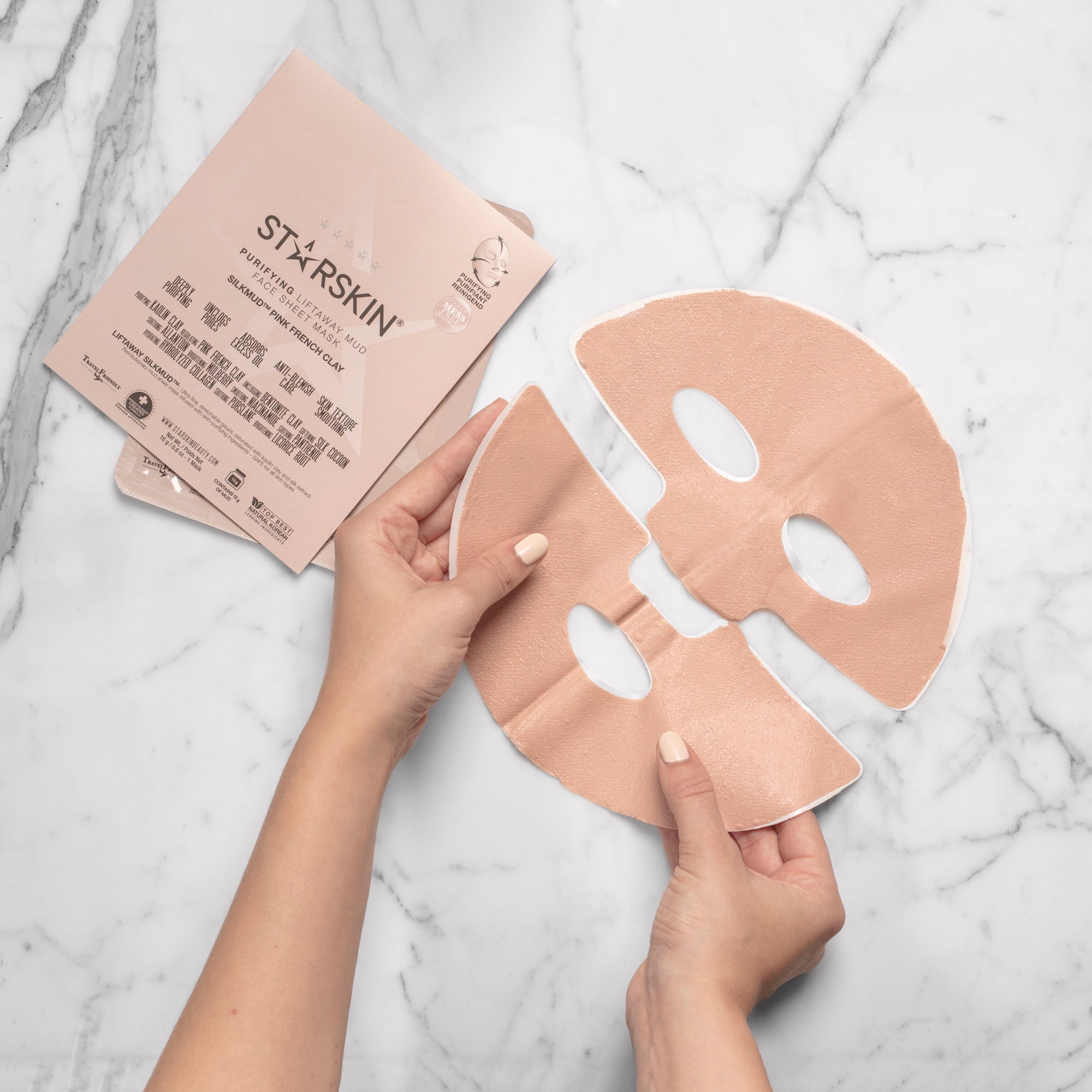 The French Pink Clay mask out of it's package. The mask is being held in someones hands. The image has a marble background