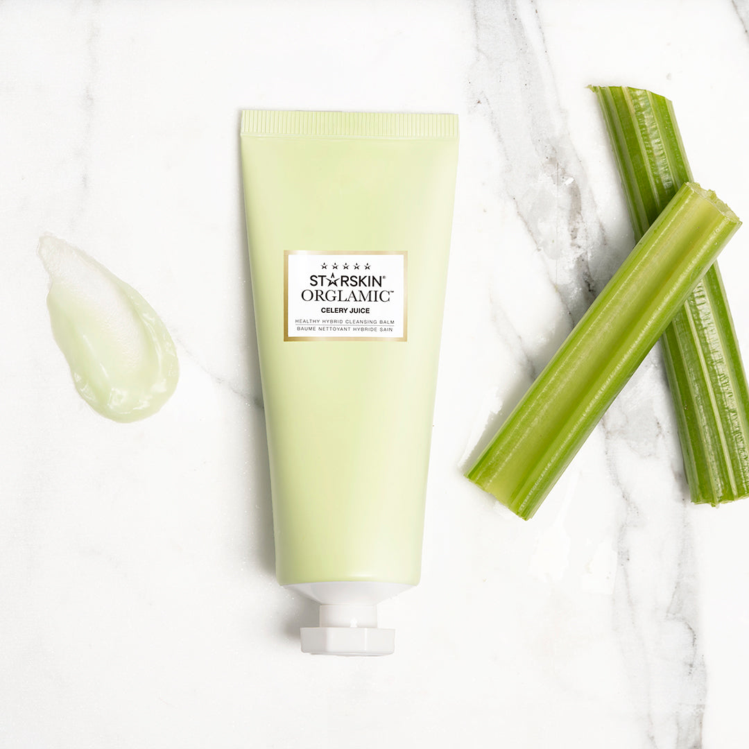 The Starskin Celery Cleansing Balm product on a marble marble background. On the right side are two celery sticks and on the left iof the product is a dot of the cleansing balm. 