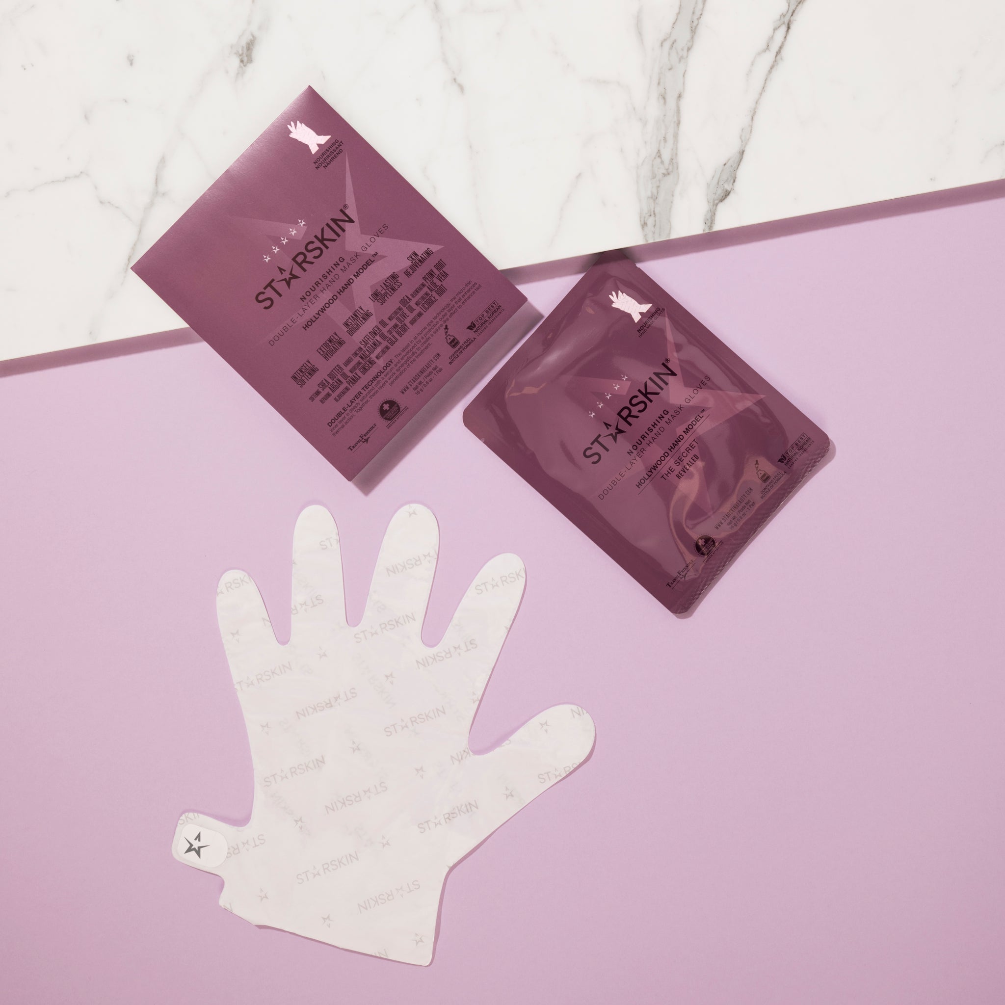 The actual product in the shape of a hand, the sachet of the product and the product packaging are all being displayed on a pink and marble colored background. 