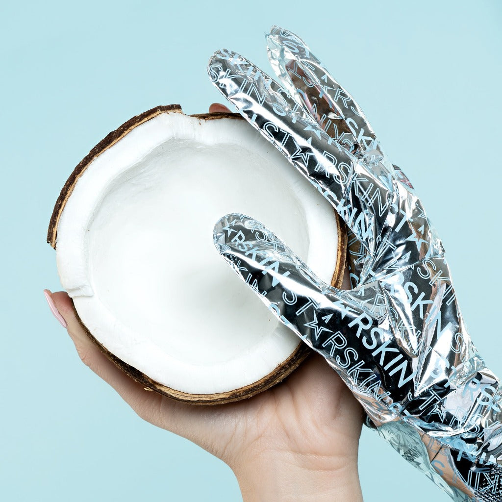 Atmospheric images of two hands. One hand holding a coconut and the other hand is wearing the STARSKIN Red Carpet Ready Hand mask while touching the coconut