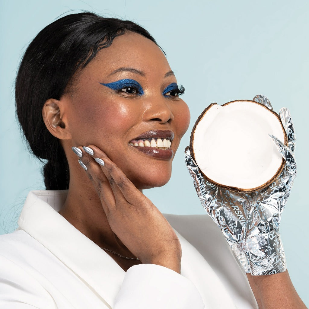 Image of a model wearing the STARSKIN Red Carpet Ready Hand Mask and holding a coconut